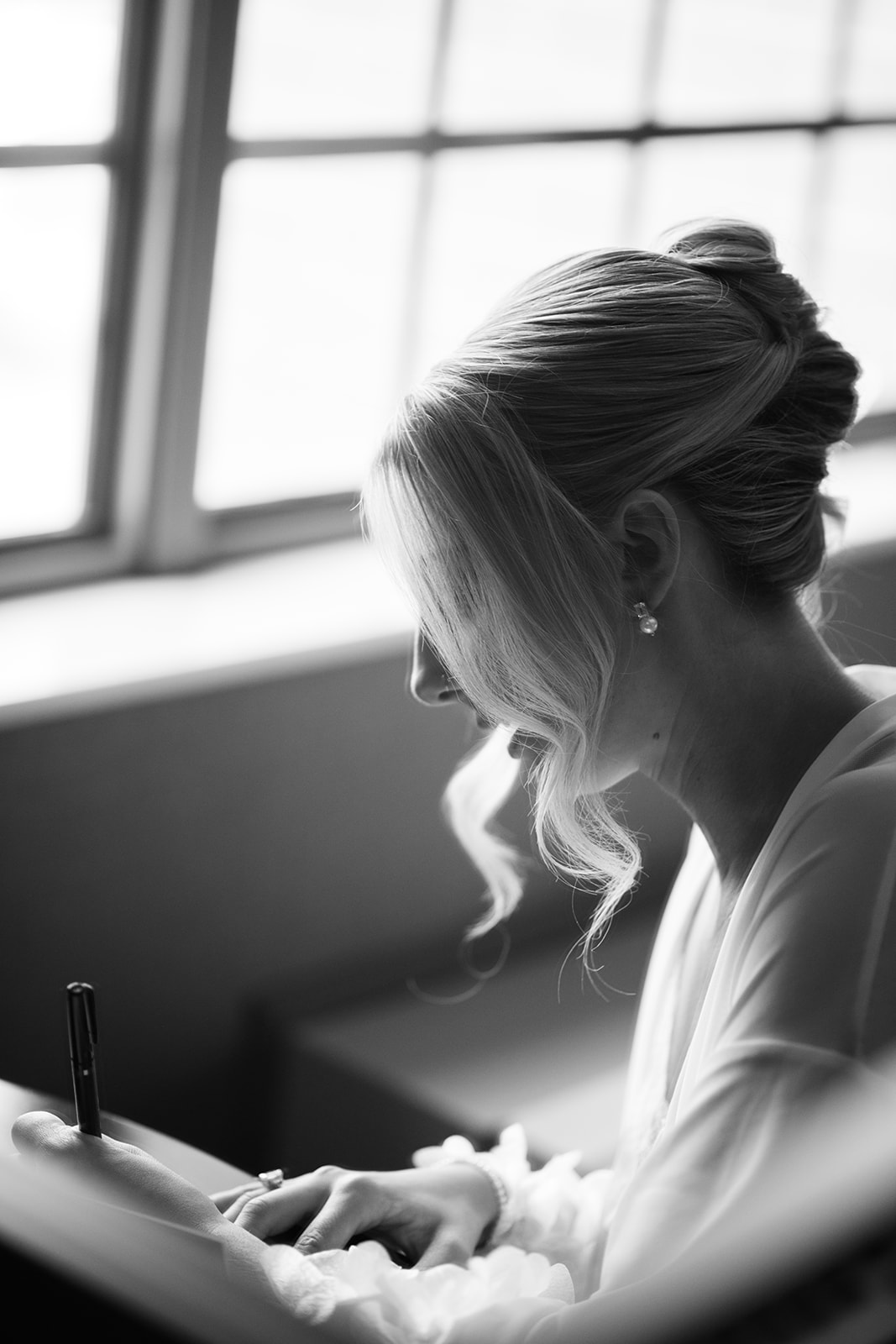 Black and white profile of the bride writing a letter, backlit by soft light from a window.
